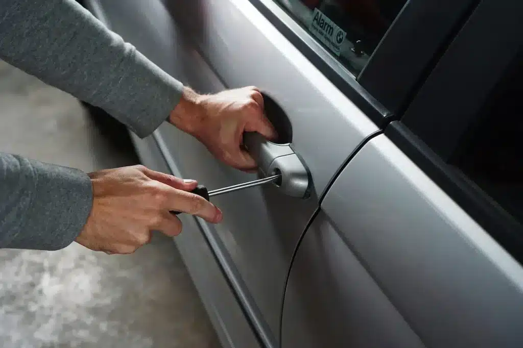 Person trying to unlock a car door with a tool during a car lockout situation.