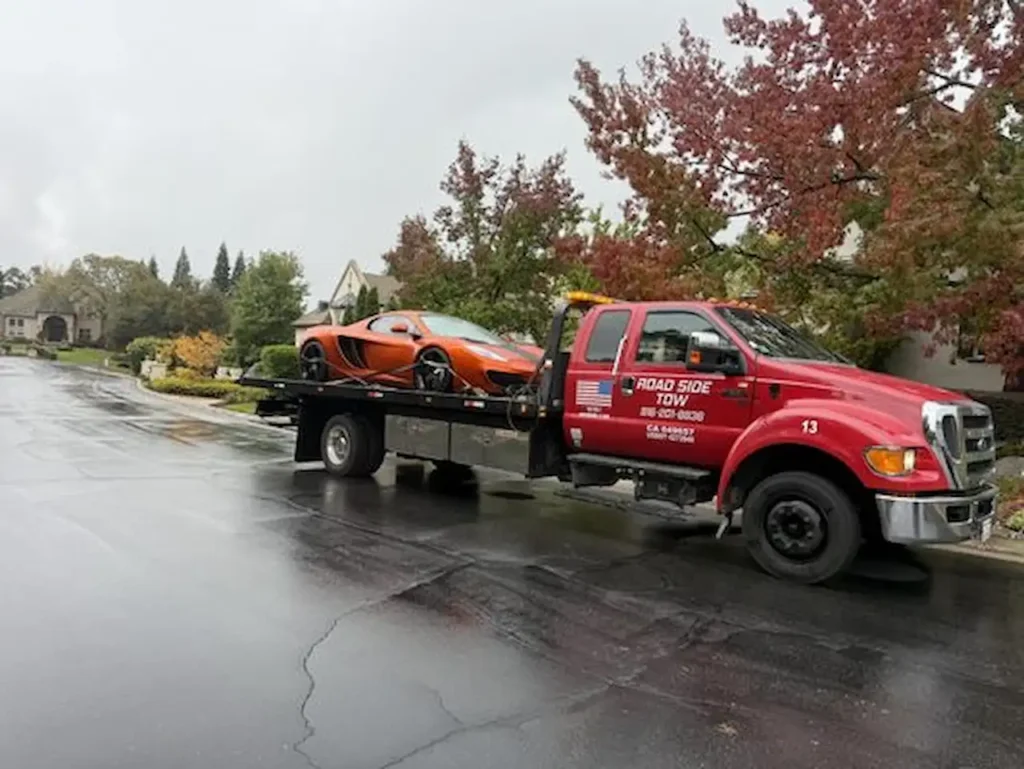 Local tow truck transporting a sports car on a flatbed in a residential area.