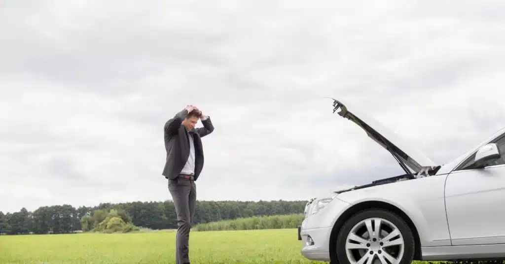 Frustrated male driver standing next to a white car with an open hood after an engine breakdown.