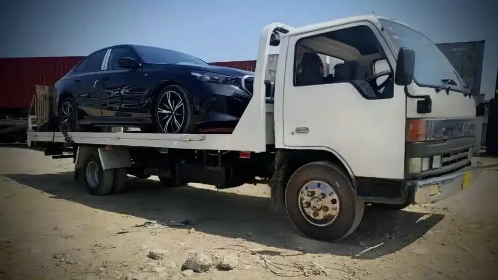 White flatbed tow truck transporting a black sedan during an emergency roadside rescue.