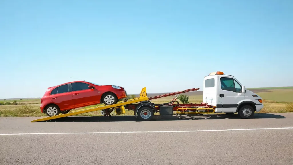 Tow truck loading a red car onto a flatbed on a roadside.