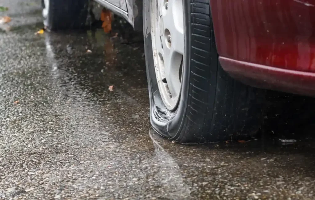 Flat car tire on a wet road during rainy weather.