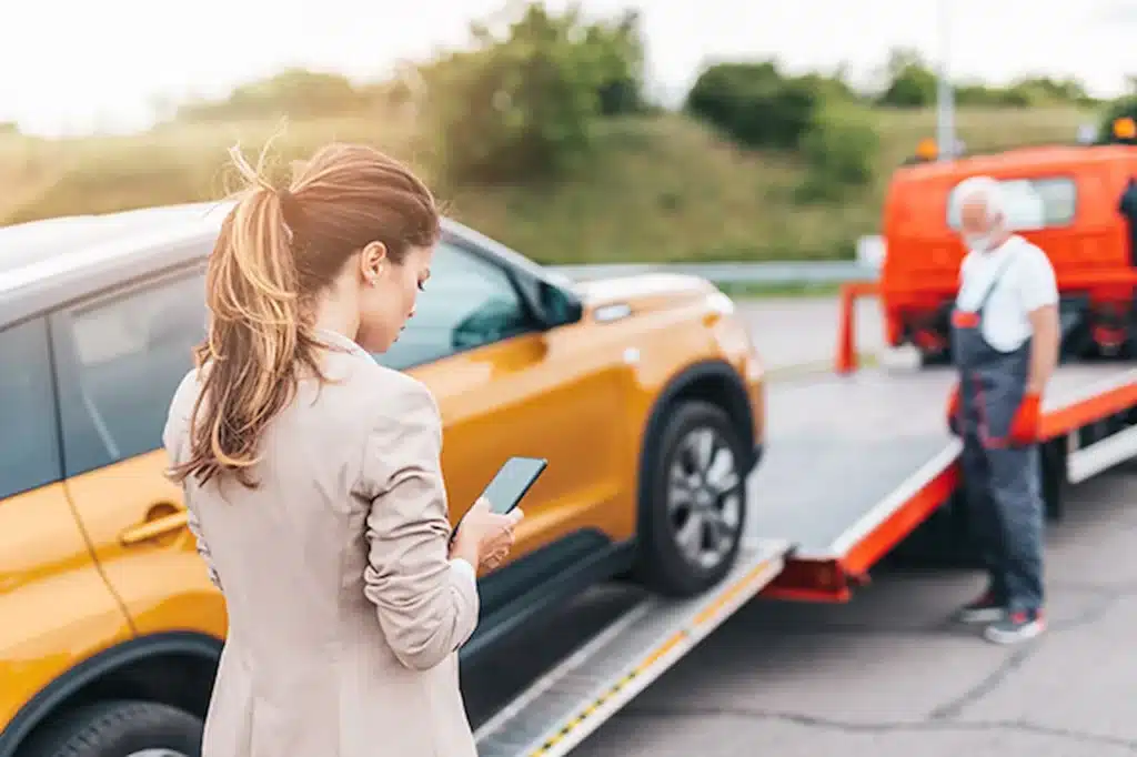 Woman using phone while her car is being loaded onto a tow truck.