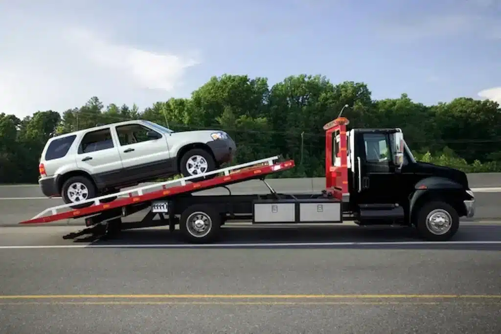 Tow truck carrying a vehicle safely on a flatbed along the road.