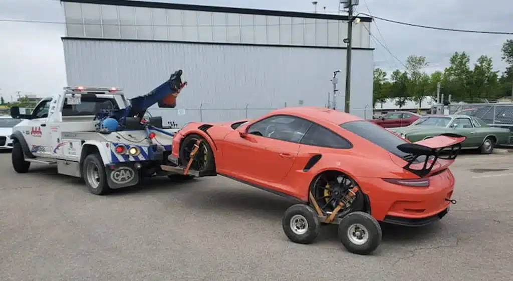 An orange sports car being safely towed with a wheel-lift truck and tow dollies to prevent drivetrain damage.